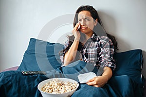 Young beautiful woman in morning bed at home. Crying during watching melodrama movie or tv series. Hold white tissue in