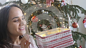 Young beautiful woman is opening xmas gift box with excited surprised face feeling happy on New Year& x27;s Eve sitting at
