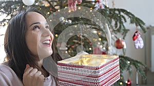 Young beautiful woman is opening xmas gift box with excited surprised face feeling happy on New Year& x27;s Eve sitting at