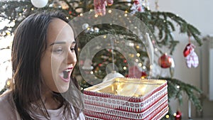 Young beautiful woman is opening xmas gift box with excited surprised face feeling happy on New Year& x27;s Eve sitting at