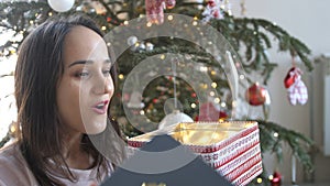 Young beautiful woman is opening xmas gift box with excited surprised face feeling happy on New Year& x27;s Eve sitting at