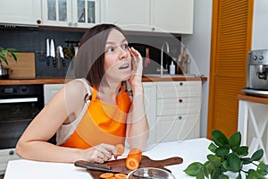 Young beautiful woman in orange apron sitting at table at kitchen background