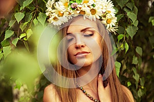 Young beautiful woman outdoor in a birchwood wearing wreth of daisy