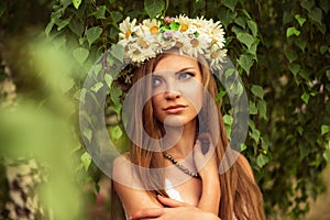 Young beautiful woman outdoor in a birchwood wearing wreth of daisy