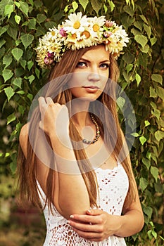 Young beautiful woman outdoor in a birchwood wearing wreth of daisy
