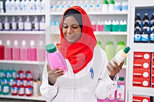 Young beautiful woman pharmacist holding shampoo bottles at pharmacy