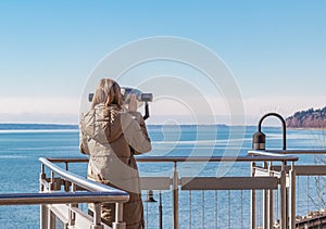Young Beautiful woman On A Pier Near The Sea Looks Through Binoculars On. Travel Search Journey Concept