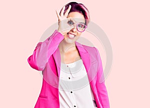 Young beautiful woman with pink hair wearing business jacket and glasses smiling happy doing ok sign with hand on eye looking