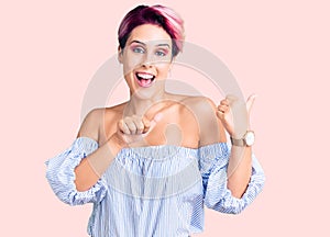 Young beautiful woman with pink hair wearing casual clothes pointing to the back behind with hand and thumbs up, smiling confident