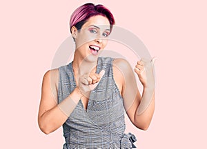 Young beautiful woman with pink hair wearing casual clothes pointing to the back behind with hand and thumbs up, smiling confident