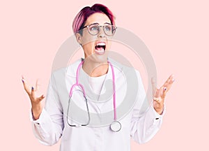 Young beautiful woman with pink hair wearing doctor uniform crazy and mad shouting and yelling with aggressive expression and arms