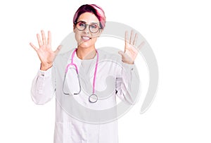 Young beautiful woman with pink hair wearing doctor uniform showing and pointing up with fingers number ten while smiling