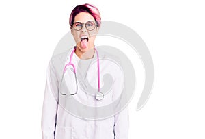 Young beautiful woman with pink hair wearing doctor uniform sticking tongue out happy with funny expression