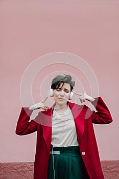 Young beautiful woman in pink headphones listening to music on pink wall background. Young gen z girl listening to music on phone