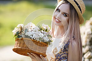 Young beautiful woman with a pleasant smile in a straw hat alone in a spring flowered park