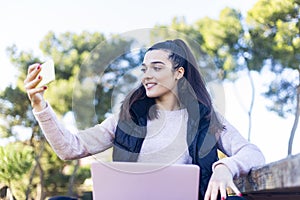 Young beautiful woman with ponytail using a smartphone outdoors to make a video conference