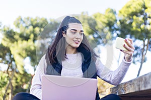 Young beautiful woman with ponytail using a smartphone outdoors to make a video conference