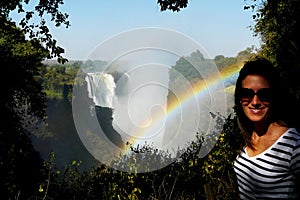 Young beautiful woman portrait with Victoria Falls on background, Zimbabwe's border line with Zambia, Africa