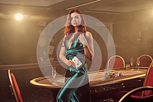 Young beautiful woman is posing against a poker table in luxury casino.