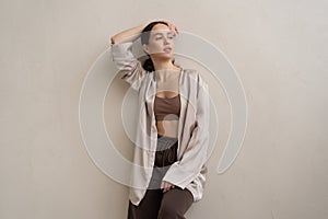 young beautiful woman posing in beige lingerie in the studio, standing near the window