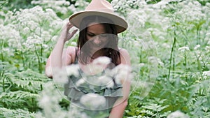 Young beautiful woman posing in a forest with a hat on a background of white flowers. happy brunette in a field of