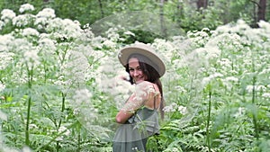 Young beautiful woman posing in a forest with a hat on a background of white flowers. happy brunette in a field of