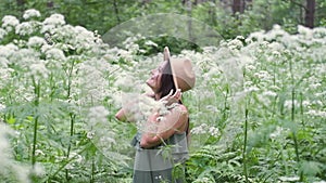 Young beautiful woman posing in a forest with a hat on a background of white flowers. happy brunette in a field of