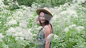 Young beautiful woman posing in a forest with a hat on a background of white flowers. Happy brunette in a field of