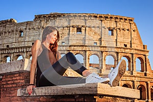 Young beautiful woman posing in front of the Colosseum. Marble arches ruins over a blue sky, Rome, Italy