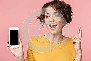 Young beautiful woman posing isolated over pink wall background using mobile phone showing display and hopeful please gesture