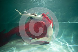 young beautiful woman posing in a red dress underwater in the pool