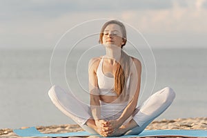 Young beautiful woman practicing yoga meditation outdoors by the sea. Yoga at sunrise on the beach