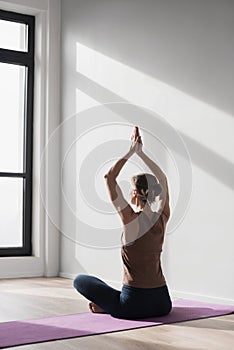 Young beautiful woman practicing yoga near floor window in yoga studio, Young beautiful girl doing exercises at home.