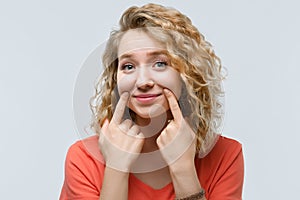 Young beautiful woman pretends to smile, stretches her mouth into a smile. Fake smile concept