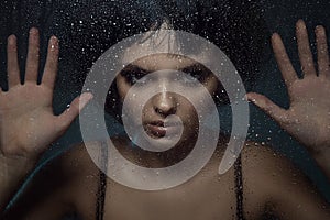 Young beautiful woman with provocative make up and stylish bob haircut standing behind the window with rain drops on it