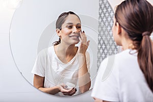 Young beautiful woman putting face cream on her nice healthy skin photo