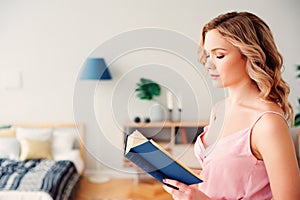 young beautiful woman reading book at home in cozy weekend morning