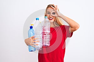 Young beautiful woman recycling plastic bottles standing over isolated white background with happy face smiling doing ok sign with