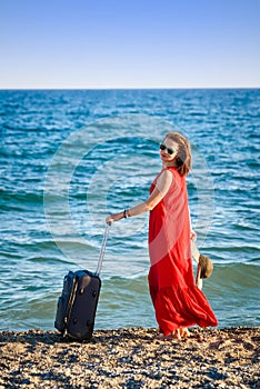 Woman in red dress with suitcase sea