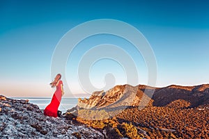 Young beautiful woman in red dress looking to mountains sea