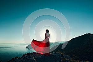 Young beautiful woman in red dress looking to mountains sea