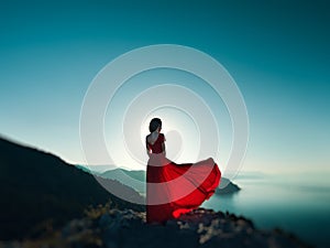 Young beautiful woman in red dress looking to mountains sea