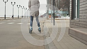 Young beautiful woman in a red hat, wearing sporty warm clothes and rollers, riding on the road on the coast