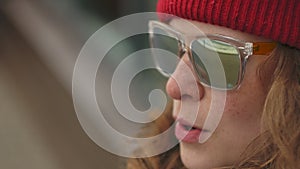 Young beautiful woman in a red hat wearing sporty warm clothes and rollers, sitting on a wooden bench drinking tea from