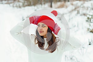 Young beautiful woman in red knitted hat and mittens in winter forest. Snowy day autdoors