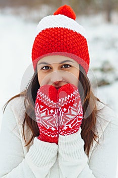 Young beautiful woman in red knitted hat and mittens in winter forest. Snowy day autdoors