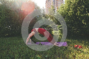 Young beautiful woman in red leggings and a top practicing yoga in a city park