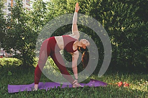 Young beautiful woman in red leggings and a top practicing yoga in a city park