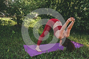 Young beautiful woman in red leggings and a top practicing yoga in a city park