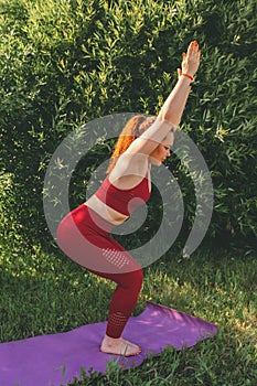 Young beautiful woman in red leggings and a top practicing yoga in a city park